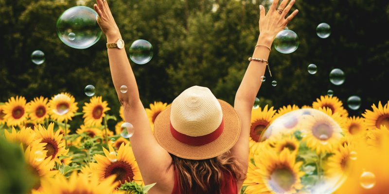 Woman excited raising her hands in the air in a field of abundance of sunflowers