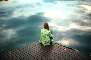 Woman with lack of drive, sitting on jetty procrastinating