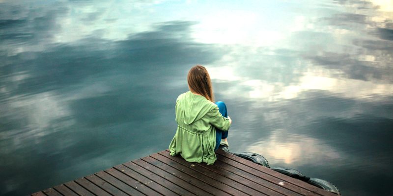 Woman with lack of drive, sitting on jetty procrastinating